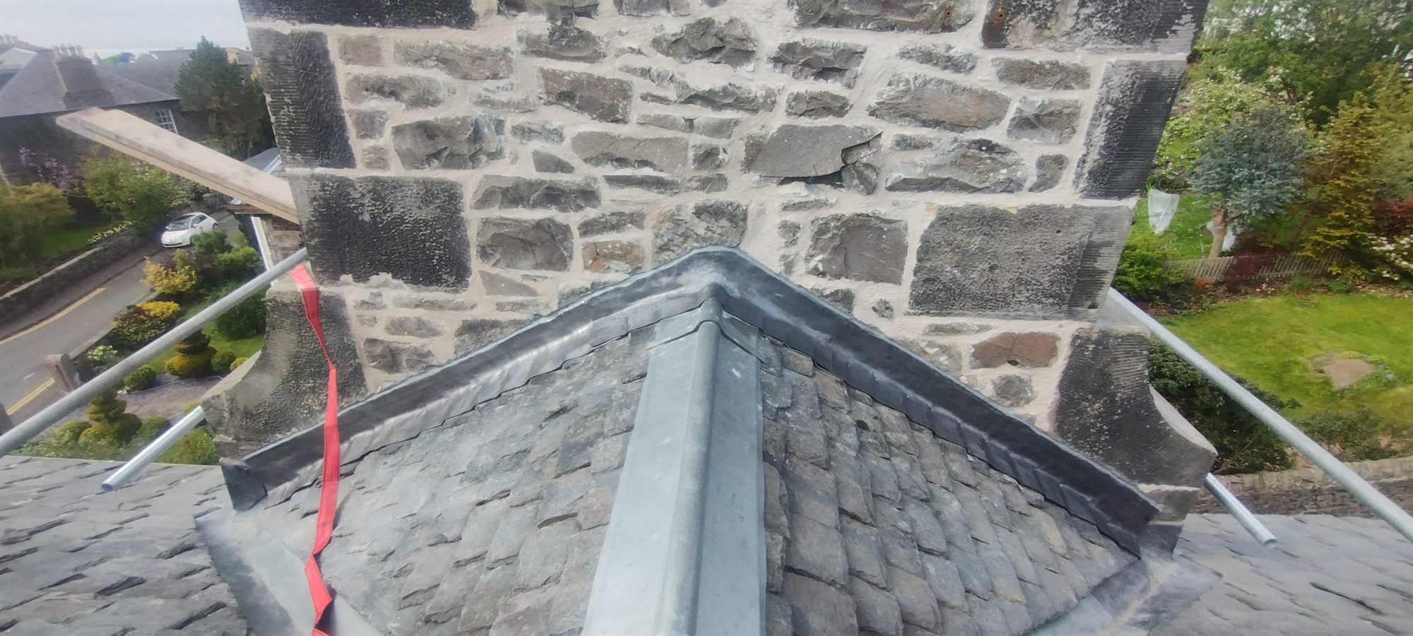 New lead ridge and hip rolls dressed over a slate roof, up against the stack.